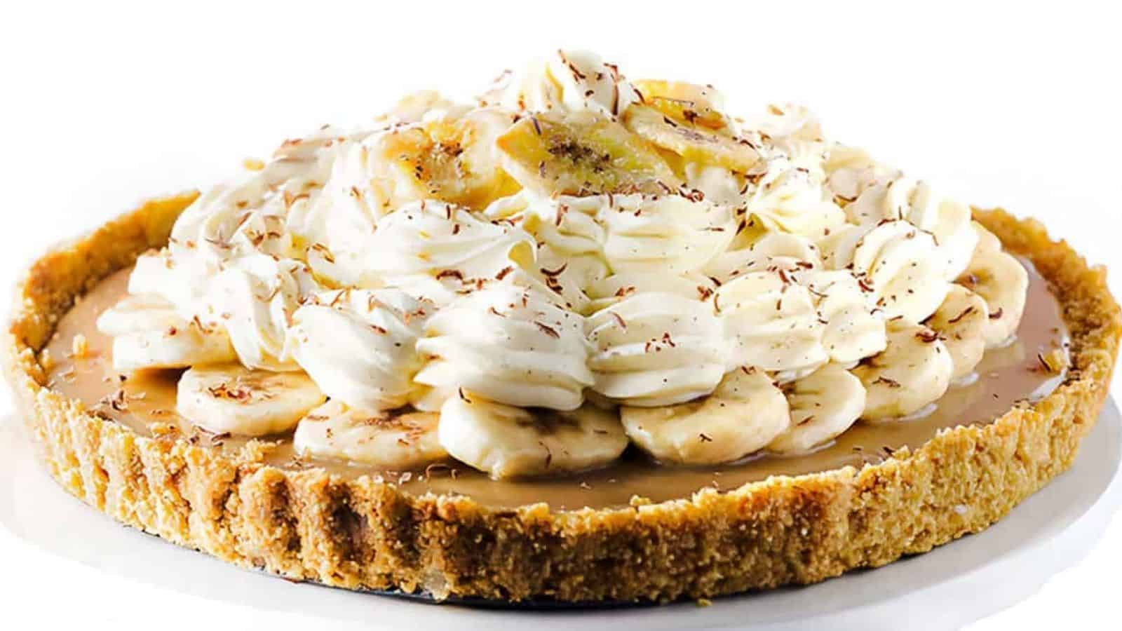 A Banoffee Pie on a cake stand showing the crust, caramel layer, banana layer, whipped cream and banana chips as decoration.