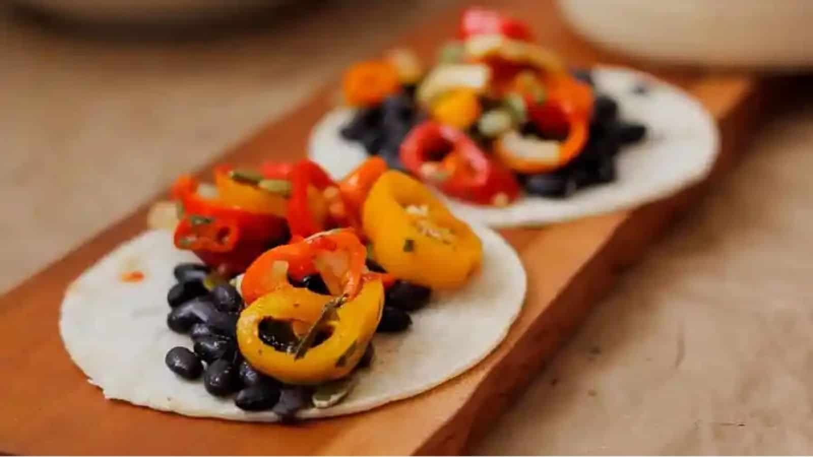 Close-up of 2 black bean tacos with sweet pepper salsa on a wooden board.