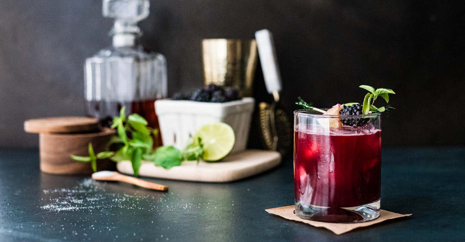 A blackberry bourbon smash in front of a cocktail bar set up.