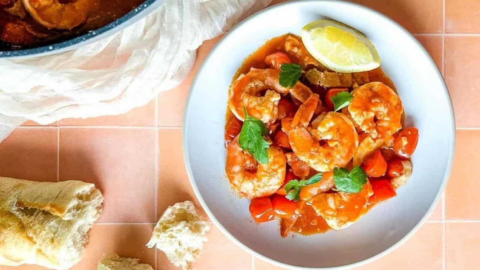 plate of bloody mary shrimp on peach tiles with a baguette.