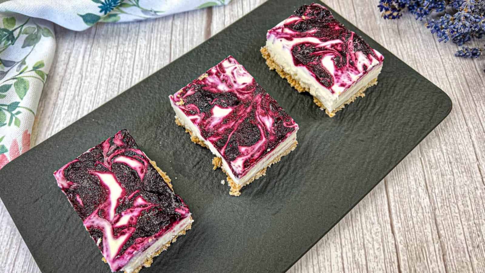 Three slices of blueberry cheesecake bars on a black slate.