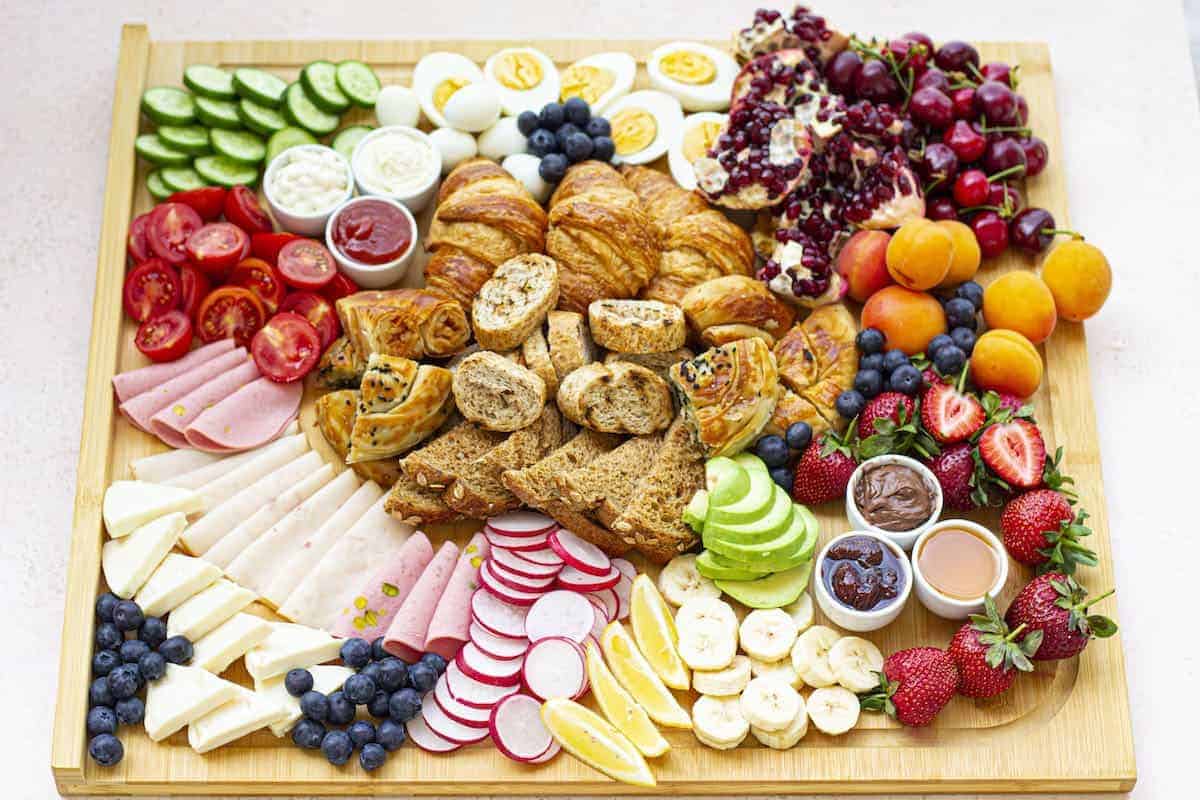 A wooden board with a variety of fruits, vegetables, and other fruits and baked goods on it.