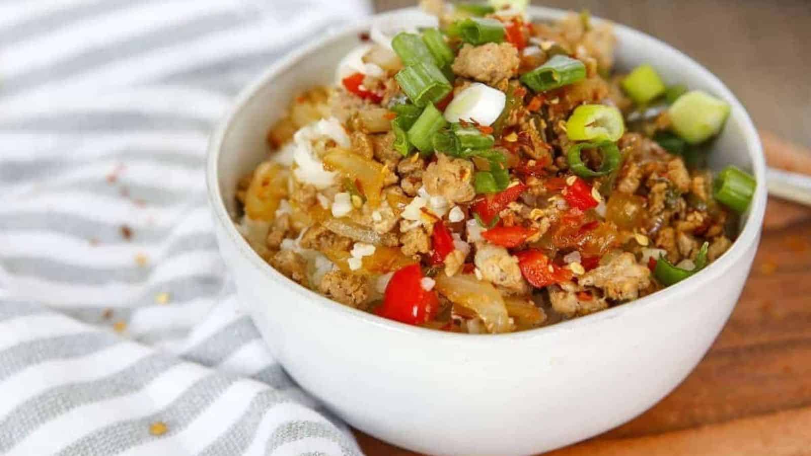 A bowl of cauliflower rice with meat and vegetables on a cutting board.