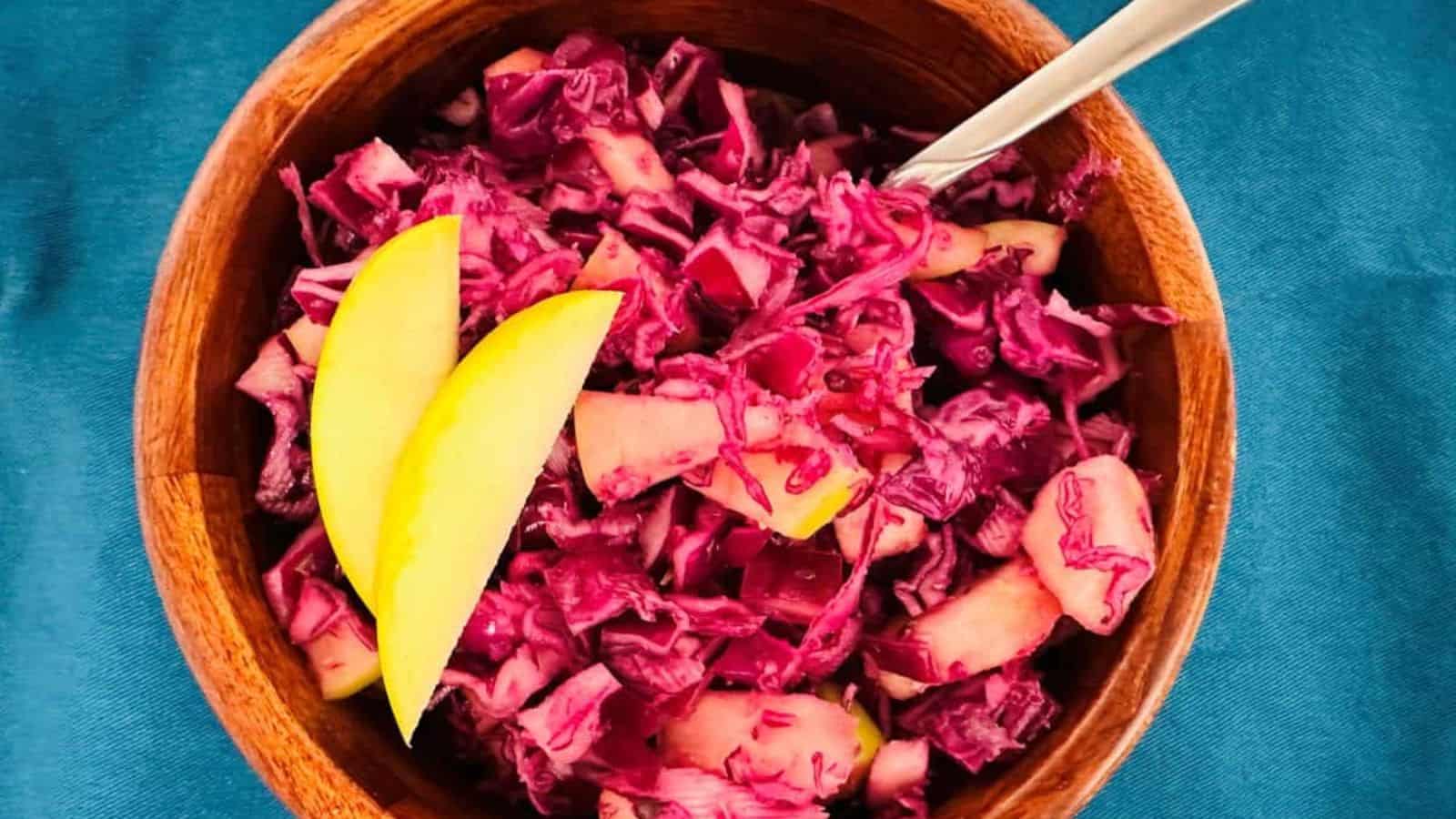 Red cabbage slaw in a wooden bowl with a spoon.