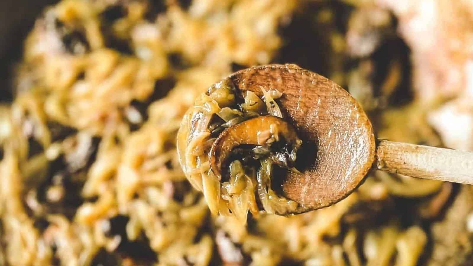 A closeup is shown of caramelized onions and mushrooms held on a wooden spoon.