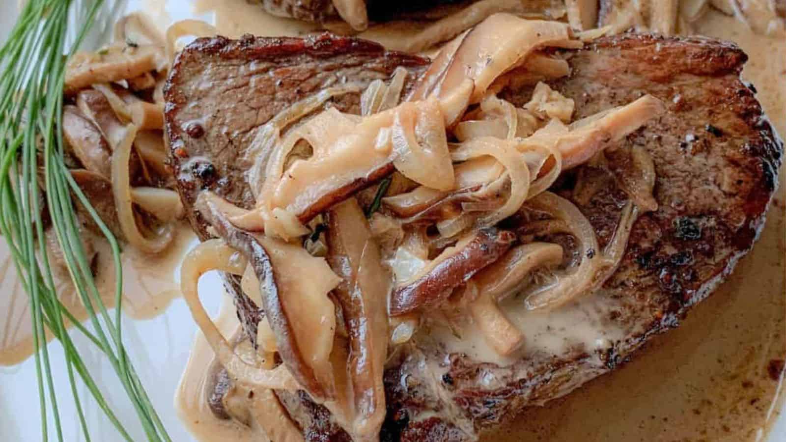 A juicy ribeye steak on a plate covered with shitake mushrooms and a creamy sauce.