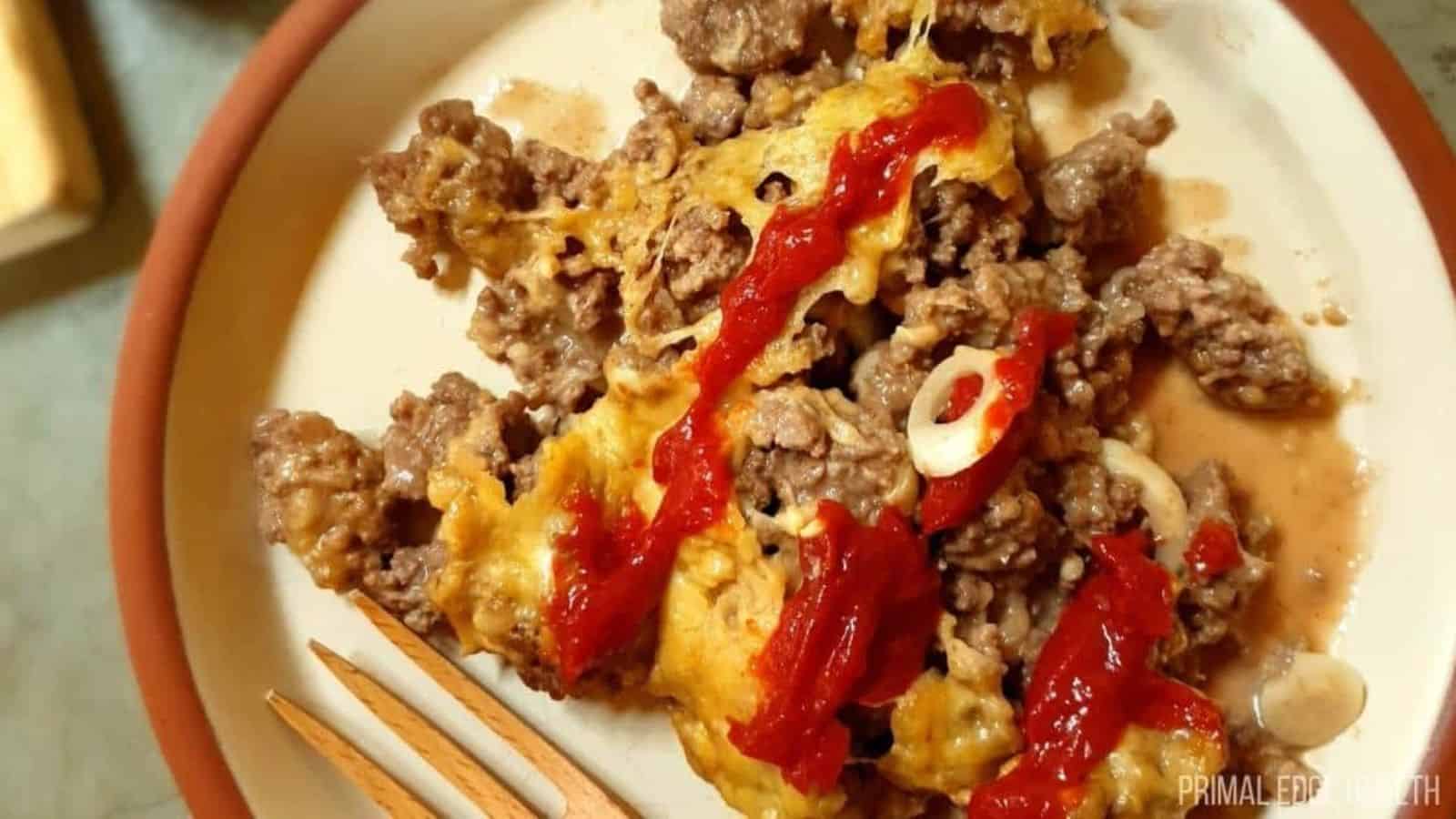 A picture of ketchup over cheesy onion and ground beef skillet dinner.