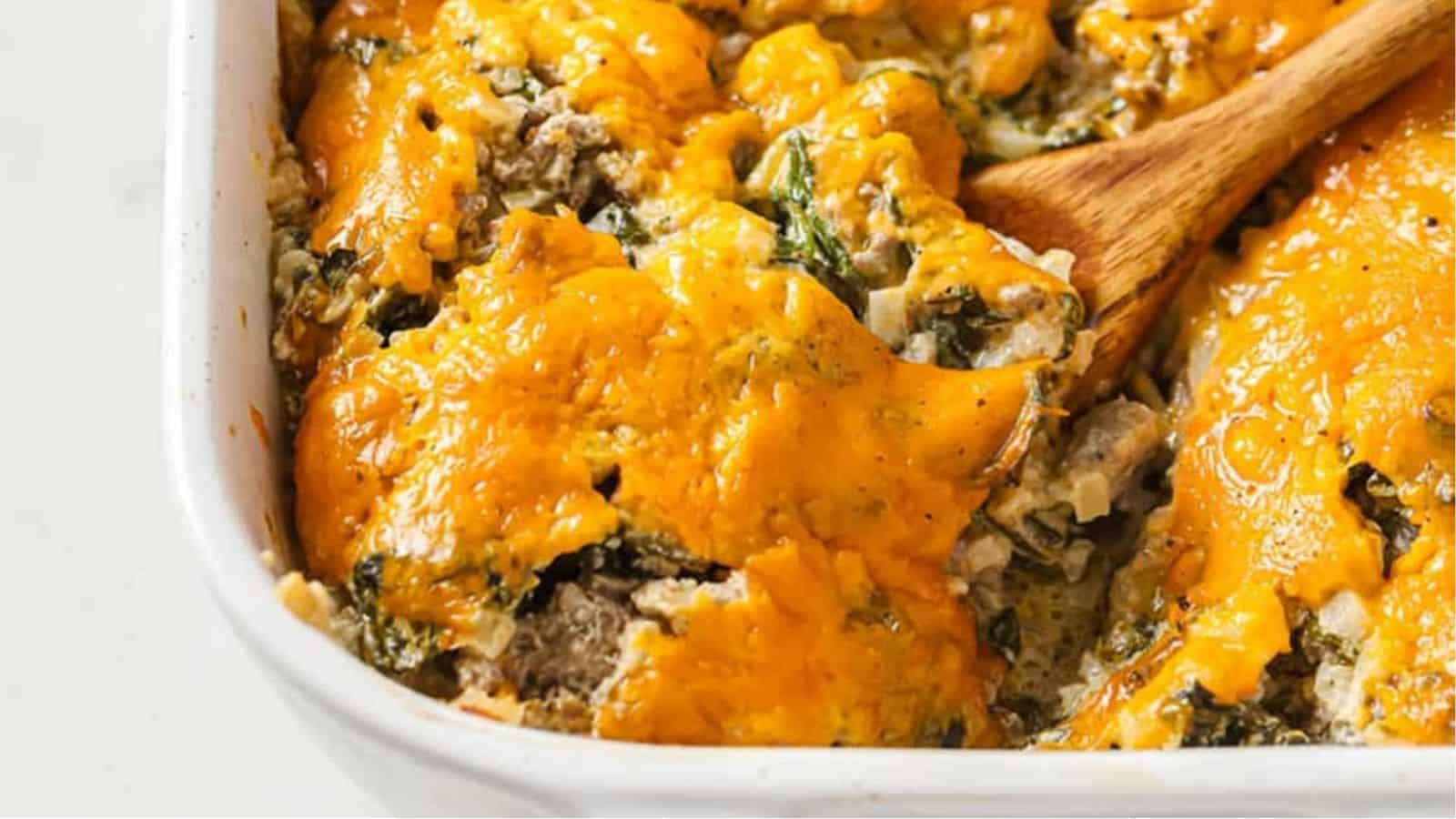 Cheesy beef casserole with cauliflower rice and spinach being spooned out of a baking dish.