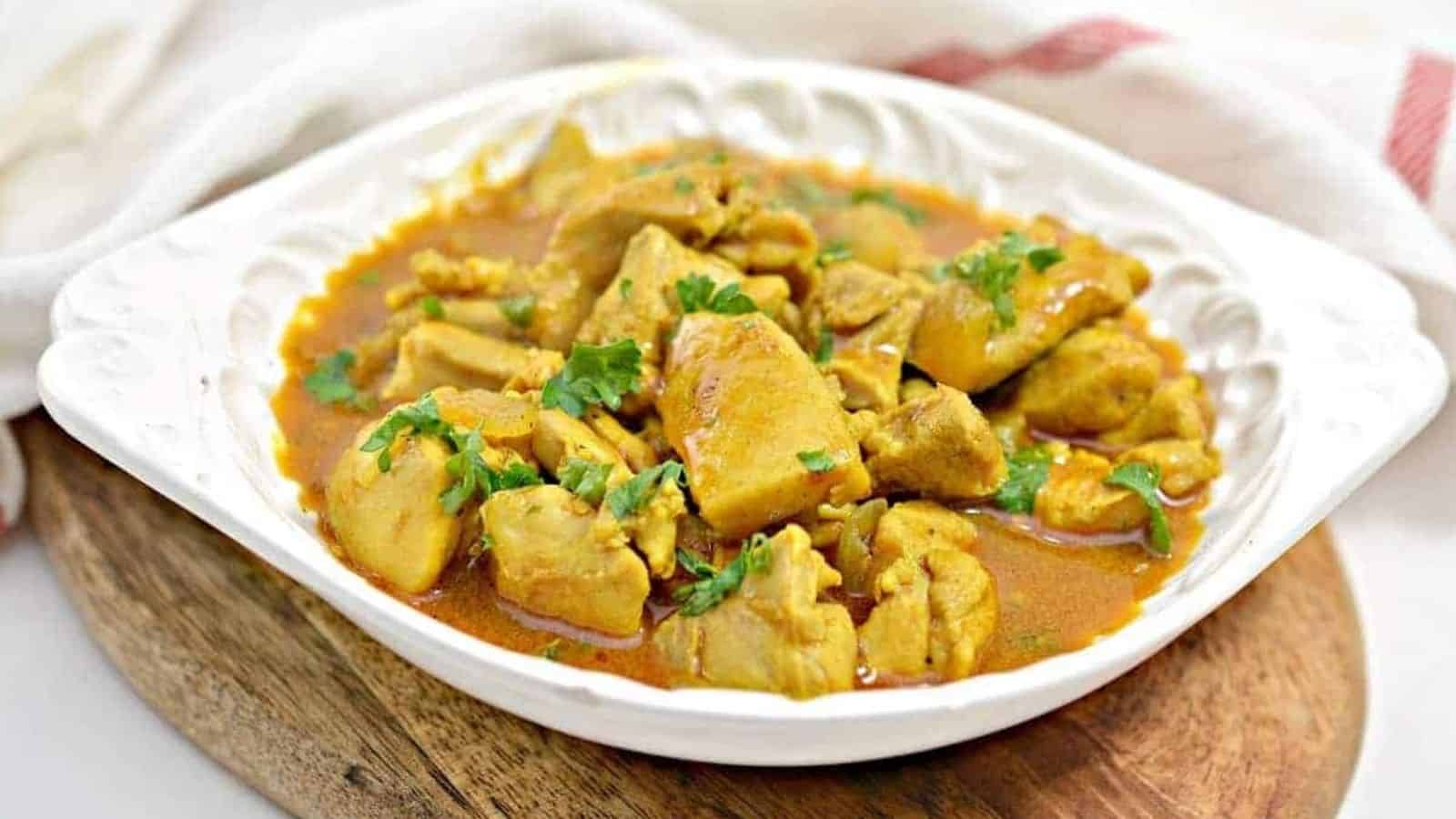 Chicken curry in a white bowl on a wooden cutting board.