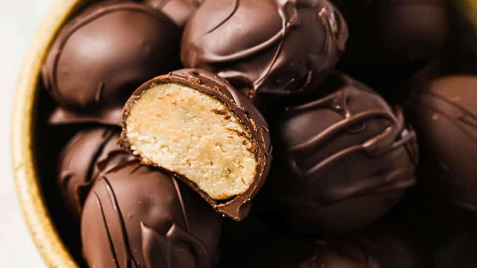 A bowl of chocolate-covered peanut butter balls with one cut in half.