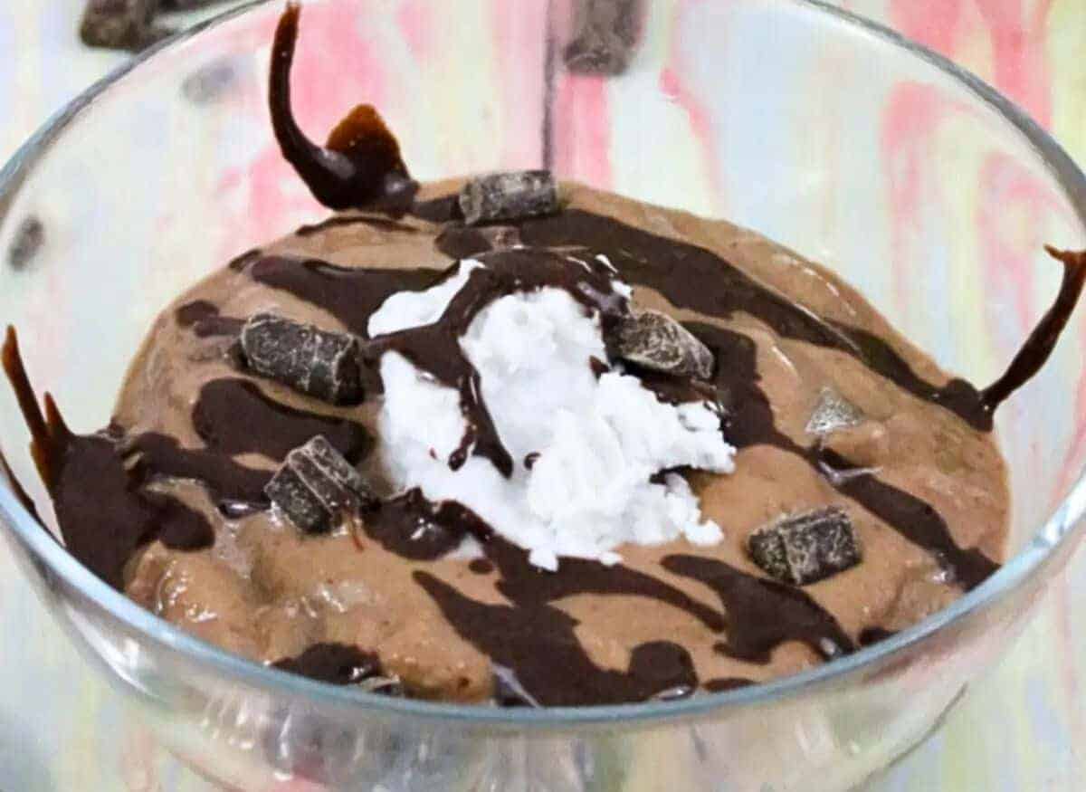 Glass bowl with chocolate protein fluff drizzled with chocolate powder and topped with whole30 whipped cream with protein powder behind it.