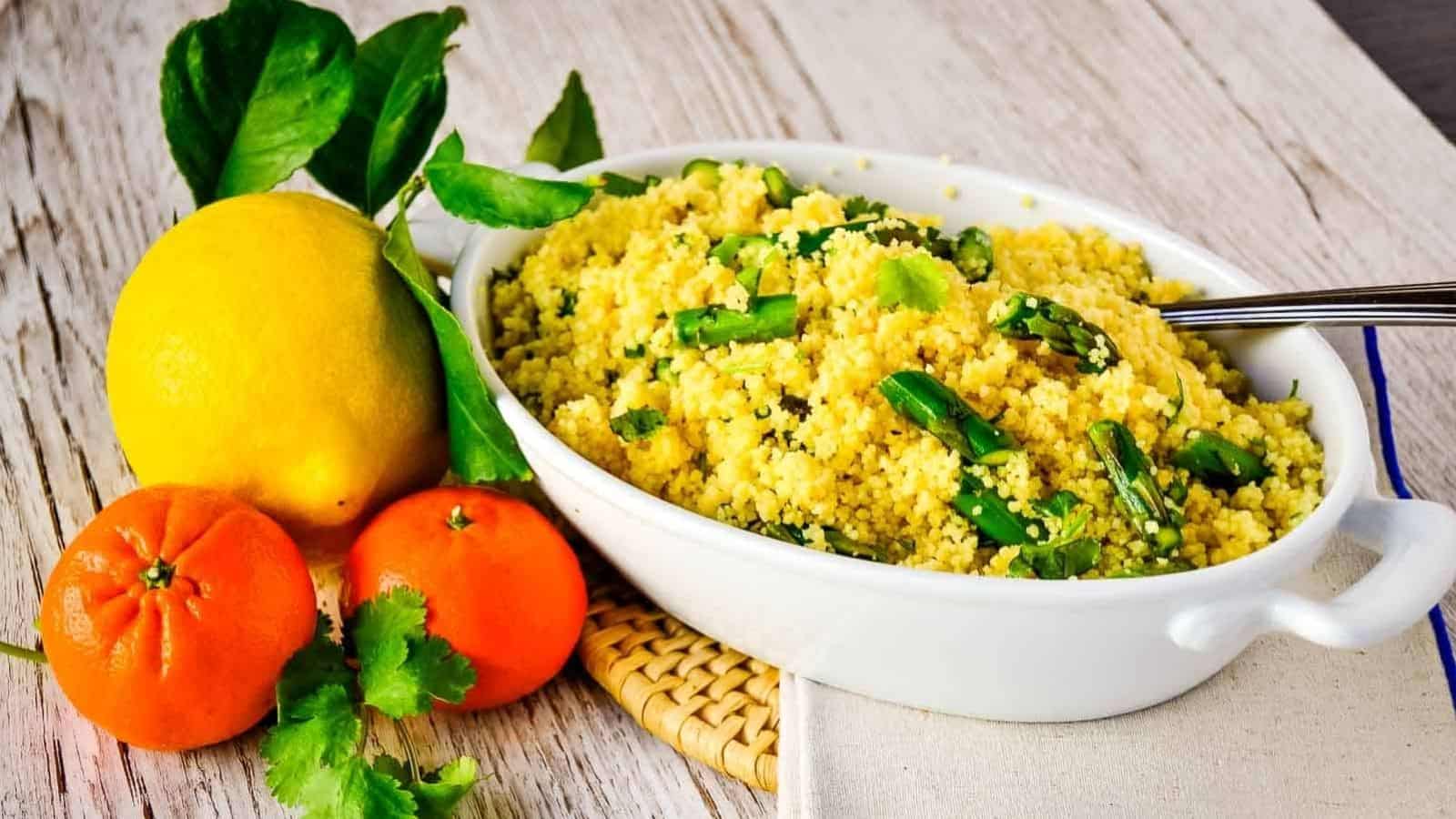 Citrus asparagus couscous in a white bowl next to an orange and lemons.