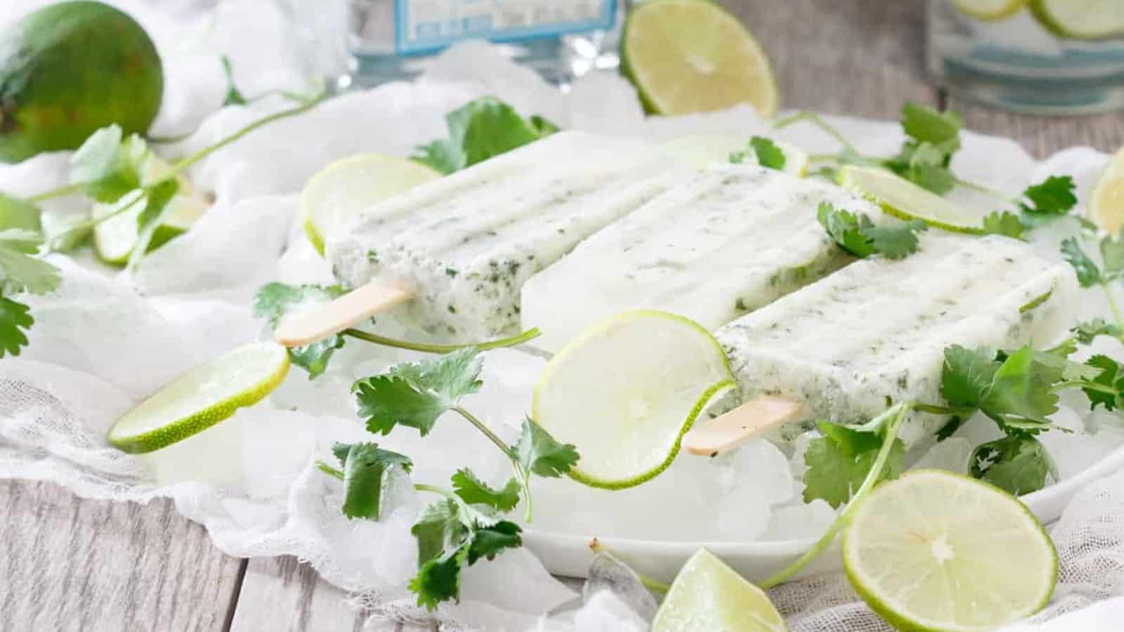 Coconut cilantro margarita ice pops on a plate of ice with fresh cilantro and some slices of lime.