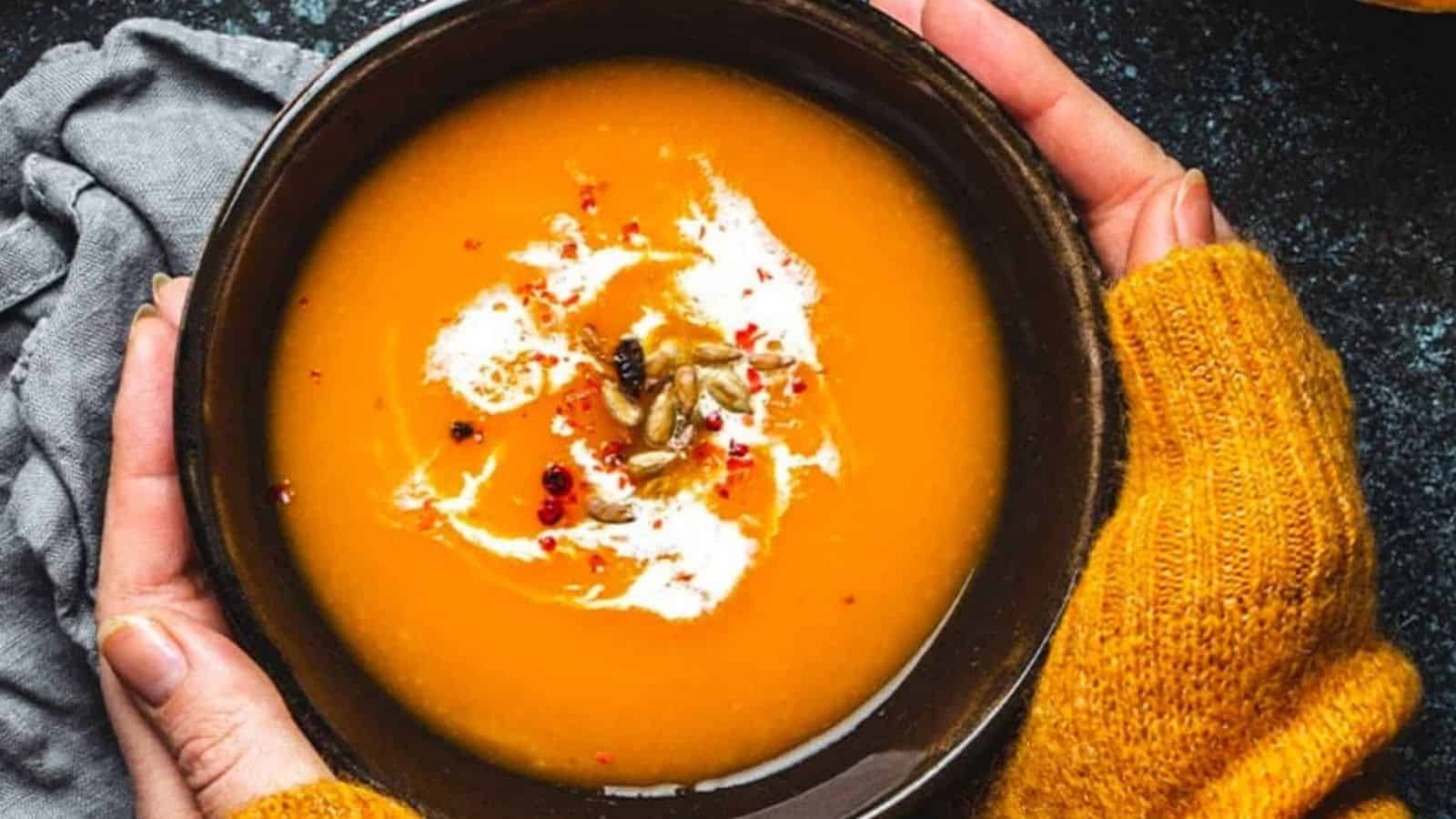 A woman holding a bowl of pumpkin soup with coconut cream.