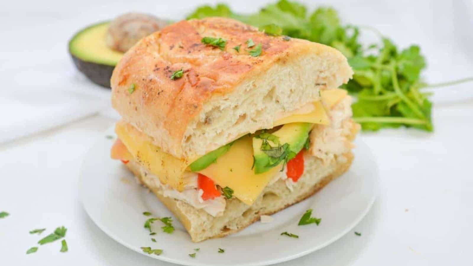 A sandwich with avocado, chicken and cheese on a plate.