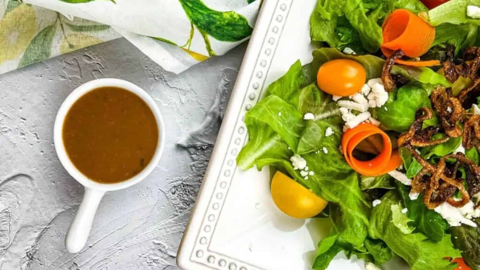 Overhead view of creamy balsamic vinaigrette in a small bowl next to a plate of salad.