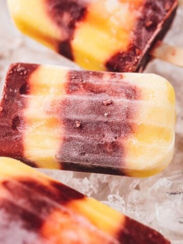 Creamy cherry mango popsicles on ice with some cherries.
