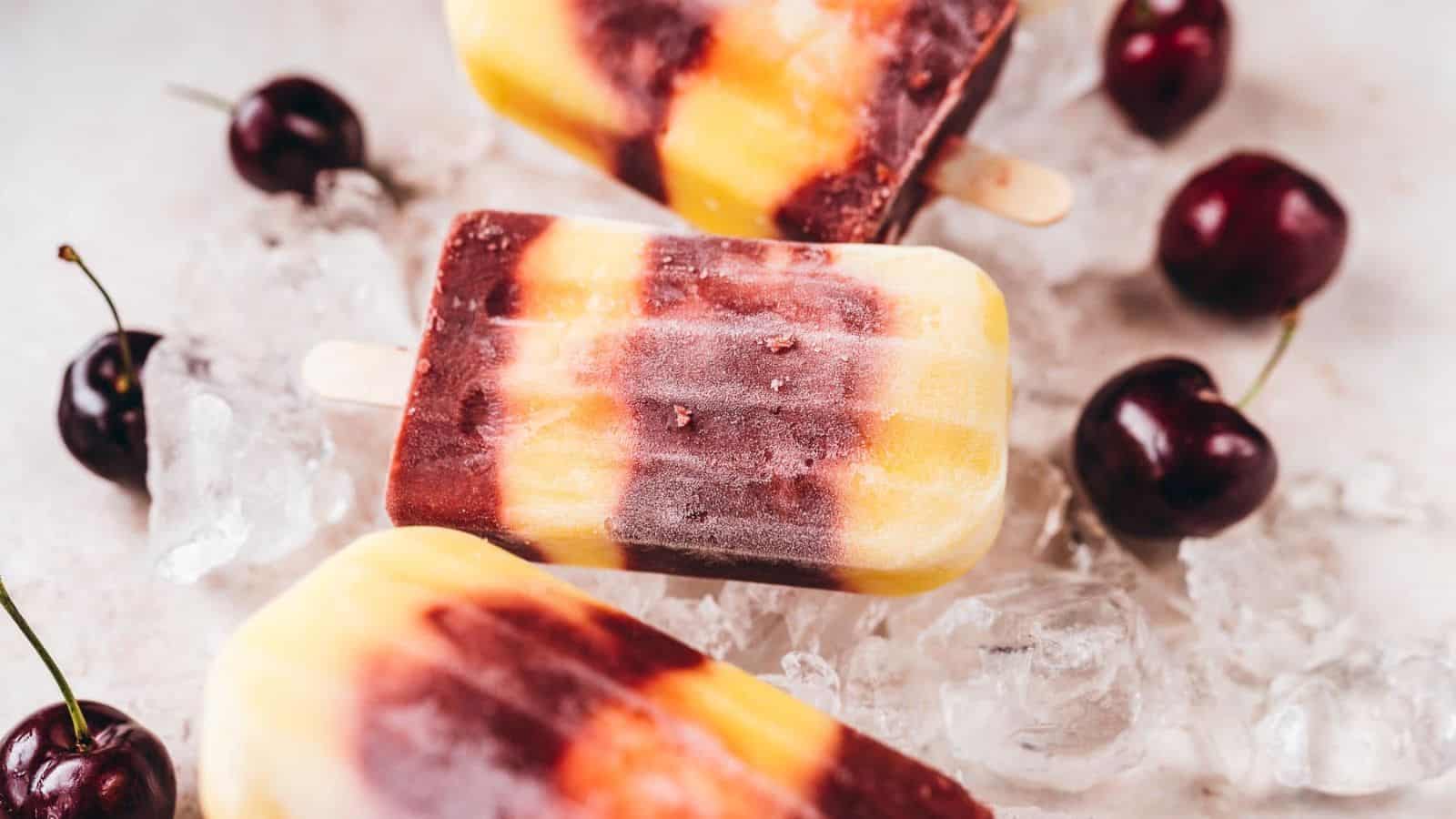 Creamy cherry mango popsicles on ice with some cherries.