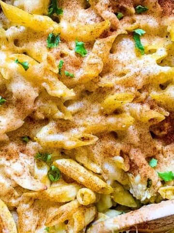 Penne and chicken in a casserole dish with pesto and cheese.