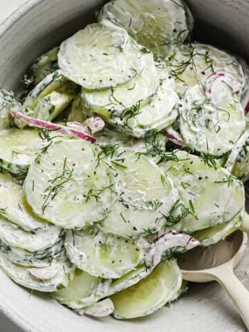 Bowl of creamy dill cucumber onion salad in a bowl with spoons.