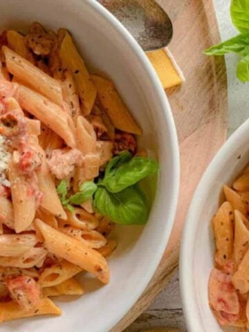 Two pasta bowls filled with penne and chunks of sausage and tomatoes.