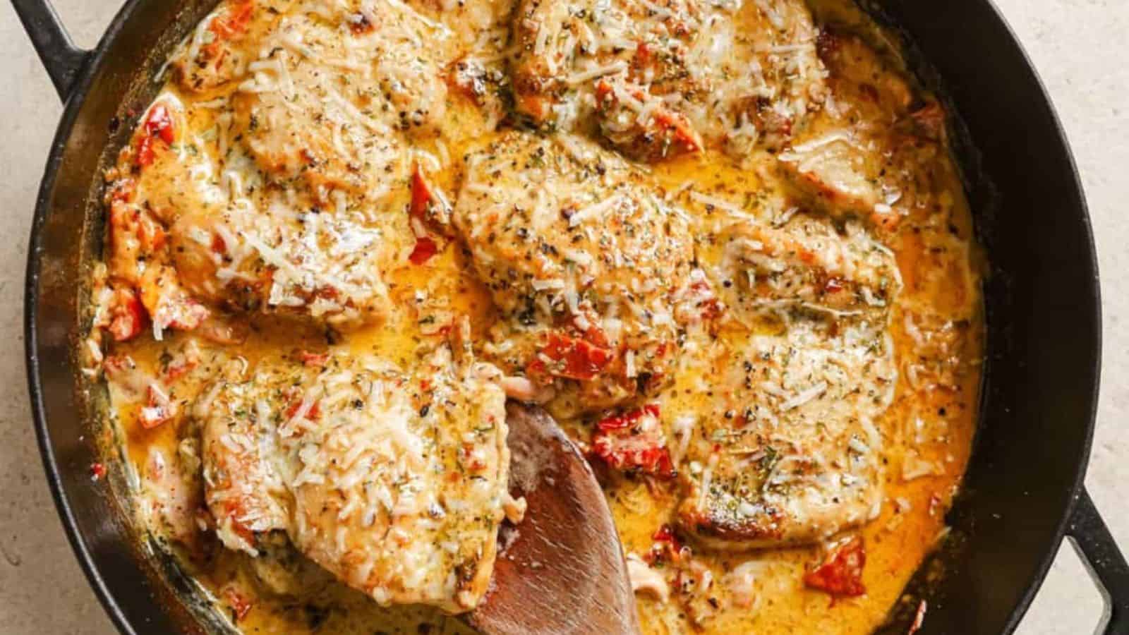 A skillet of creamy sun dried tomato chicken with a wooden spoon.