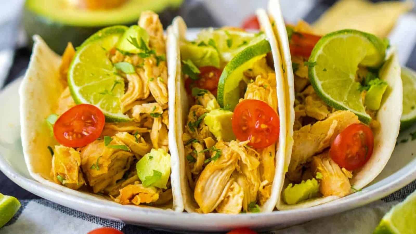 Three slow cooker tacos with chicken, lime, avocado and tomatoes.