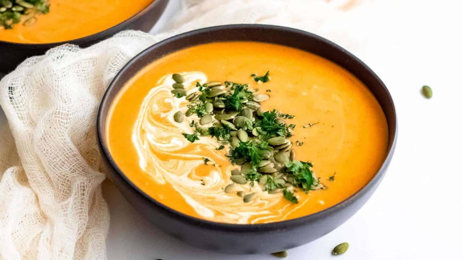 Two bowls of curry pumpkin soup with coconut cream and pumpkin seeds.