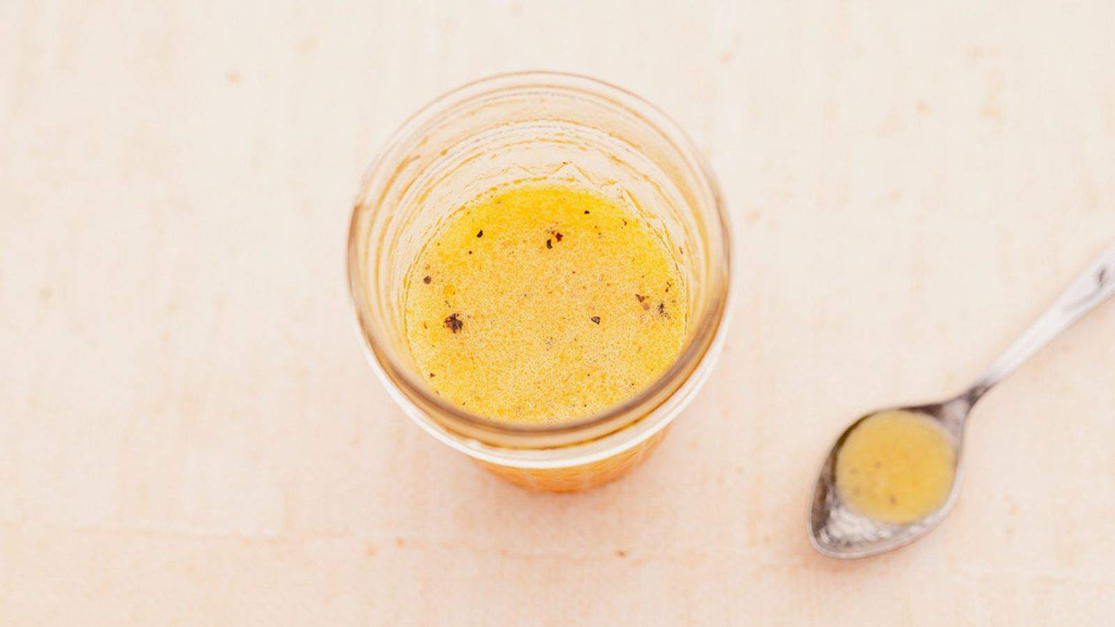 Overhead view of citrus vinaigrette salad dressing in a glass with a spoonful next to it.