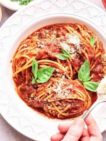 Someone sprinkling parmesan cheese on a spaghetti marinara.