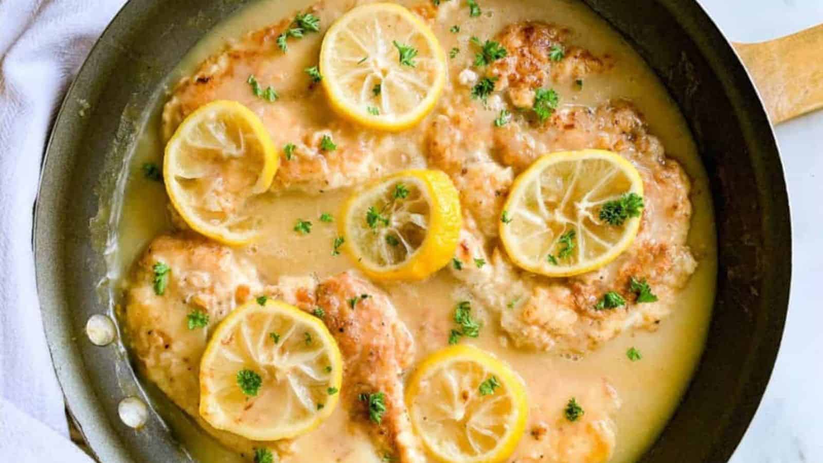 A skillet filled with lemon chicken in sauce with lemon slices.