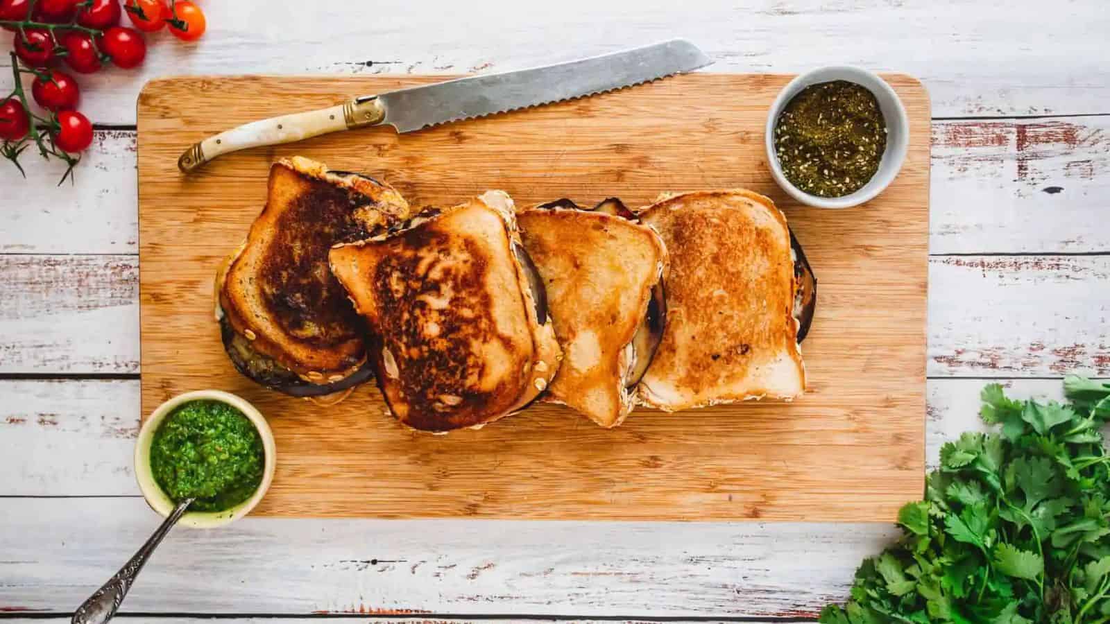 Four eggplants grilled cheese with Yemenite green hot sauce on a wooden board.