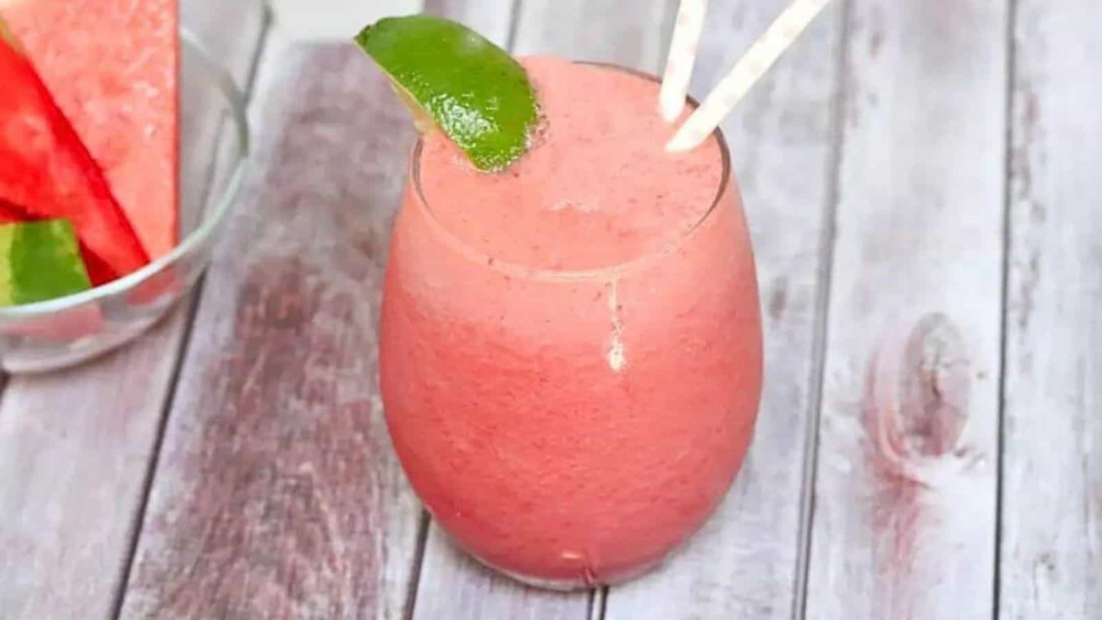 Pink watermelon slushie in a glass garnished with lime and more watermelon and lime behind it.