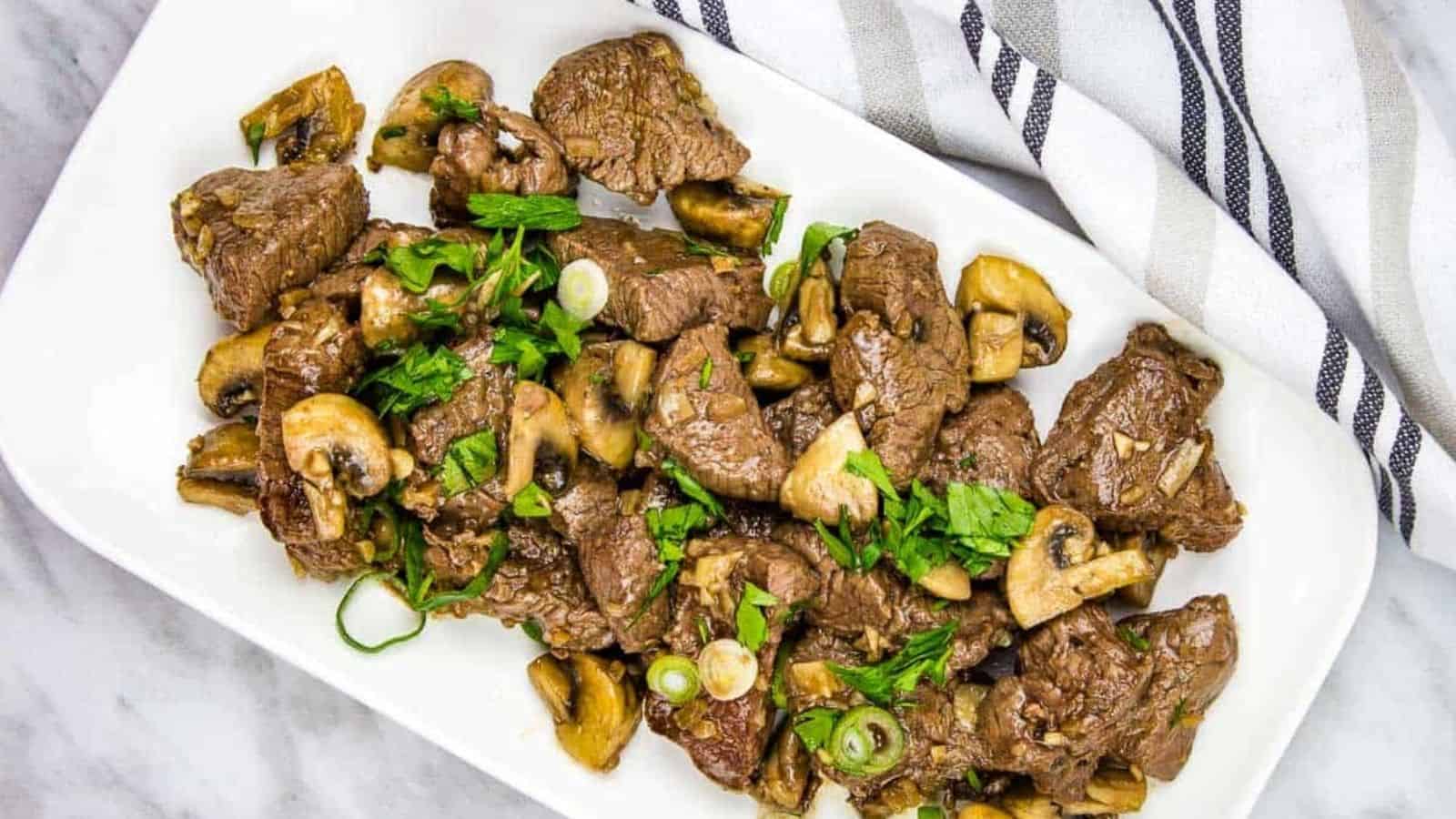 A white plate with garlic steak bites and mushrooms on it.