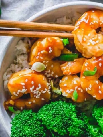 Homemade general tso shrimp with broccoli and rice in a bowl with chopsticks.