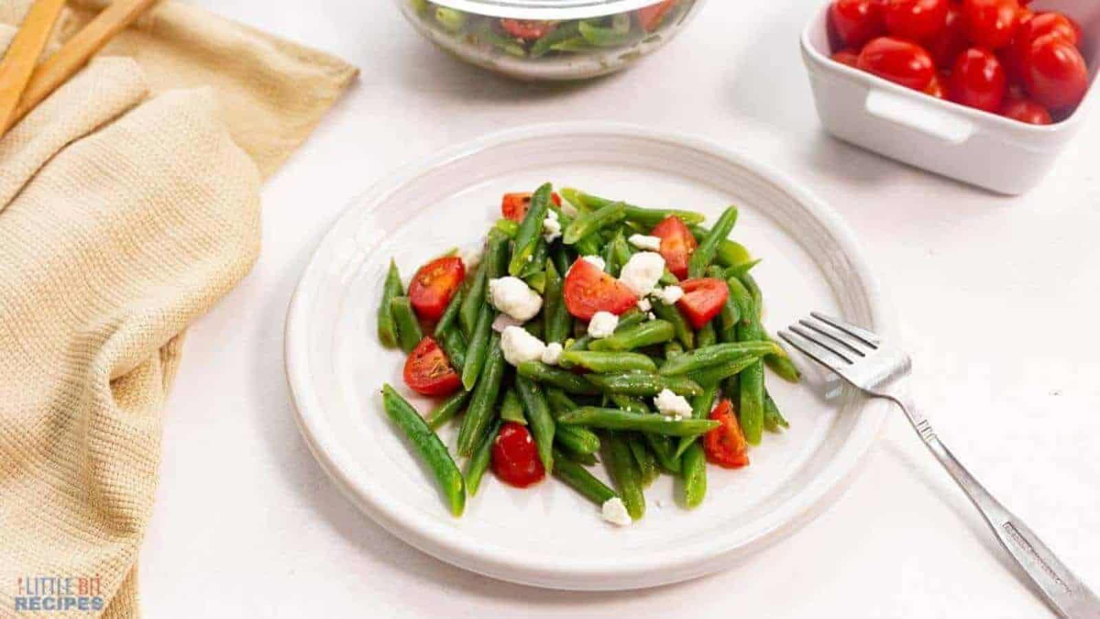 Green beans and tomatoes on a white plate.