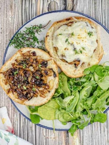 An open grilled French onion pork burger on a plate with greens.