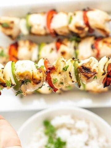 Someone holding a grilled pepper and chicken kebab.