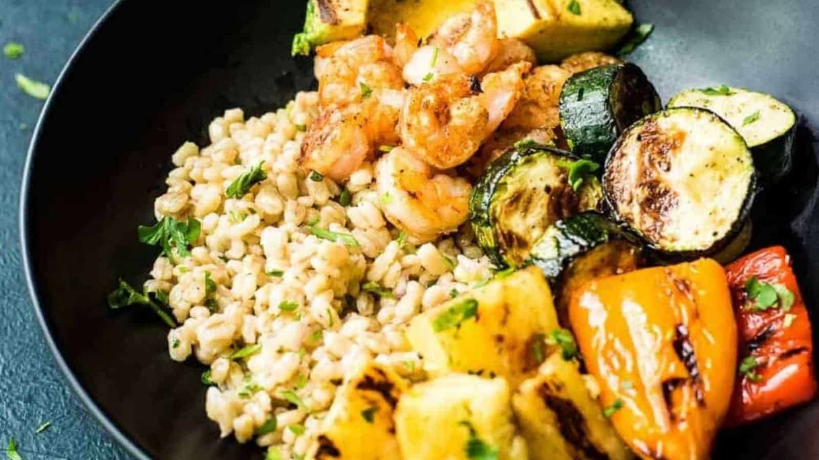 Overhead shot of shrimp skewers and veggie skewers next to a bowl of dressed grains.