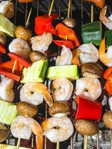 Skewers of vegetables and shrimp on a grill.
