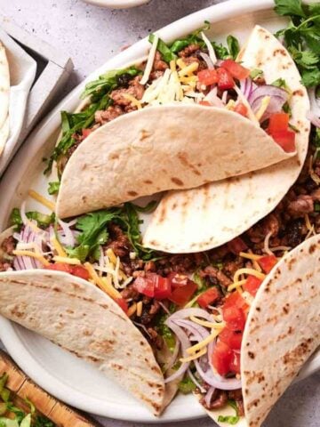 A top view of ground beef tacos on a white plate.