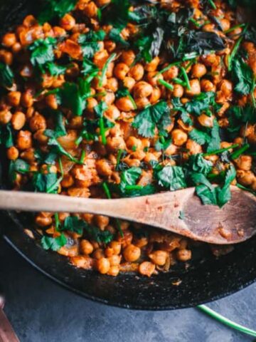 An image of Herbed Orange Harissa Chickpeas with fresh herbs on the background.