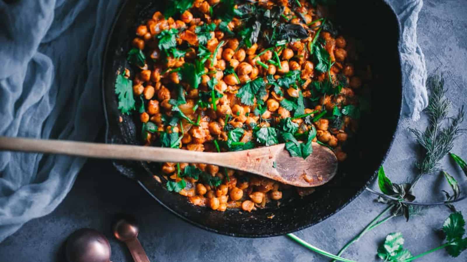 An image of Herbed Orange Harissa Chickpeas with fresh herbs on the background.