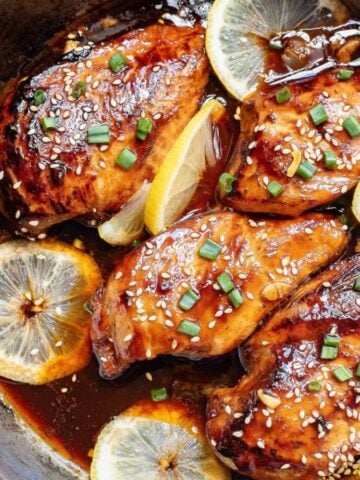 Asian glazed chicken in a skillet with lemon slices.