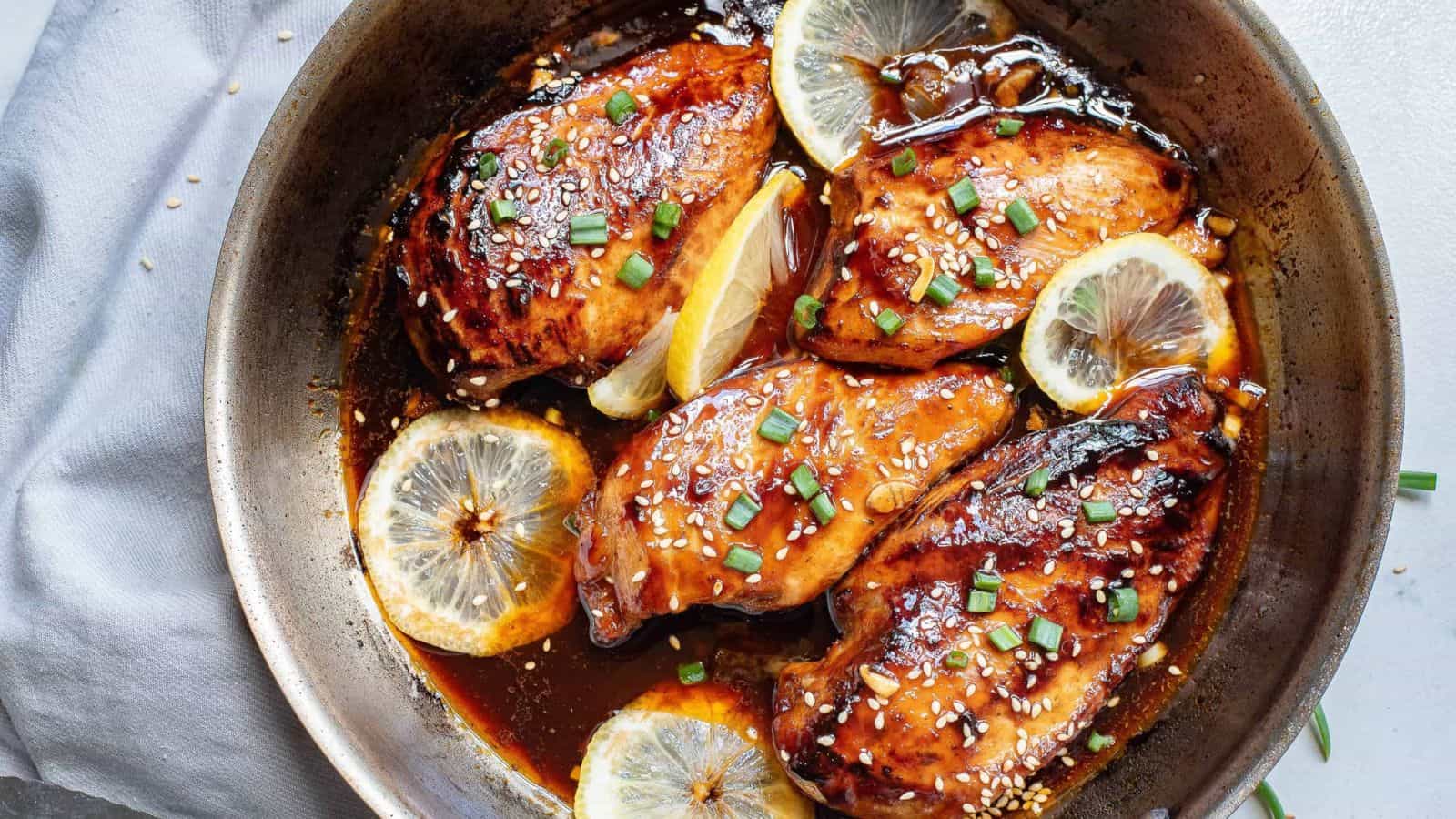 Asian glazed chicken in a skillet with lemon slices.