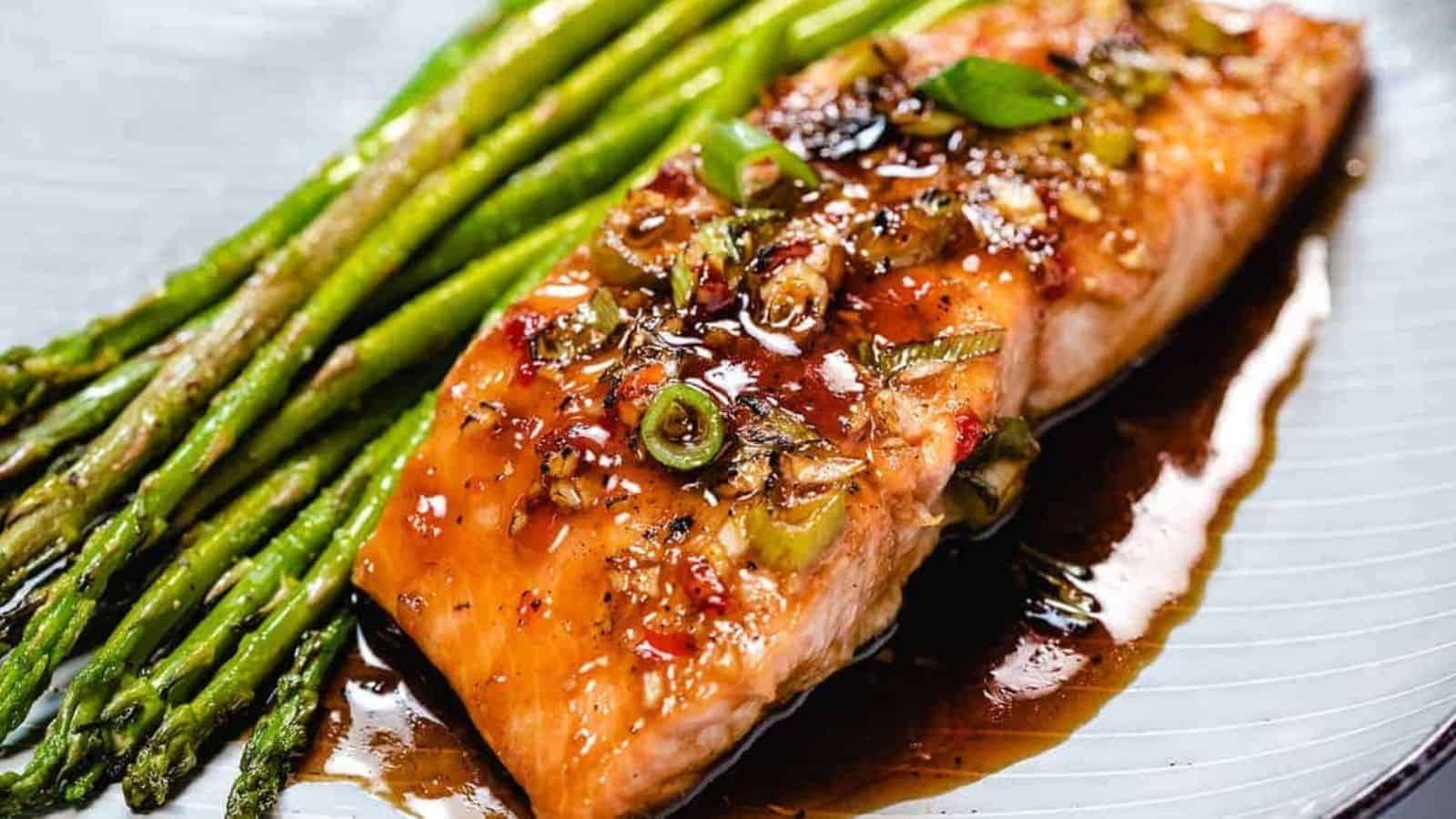 Glazed salmon on a plate with asparagus next to it.