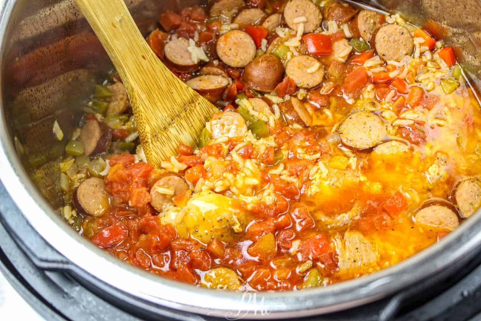 Chicken, sausage, and rice in instant pot with wooden spoon.