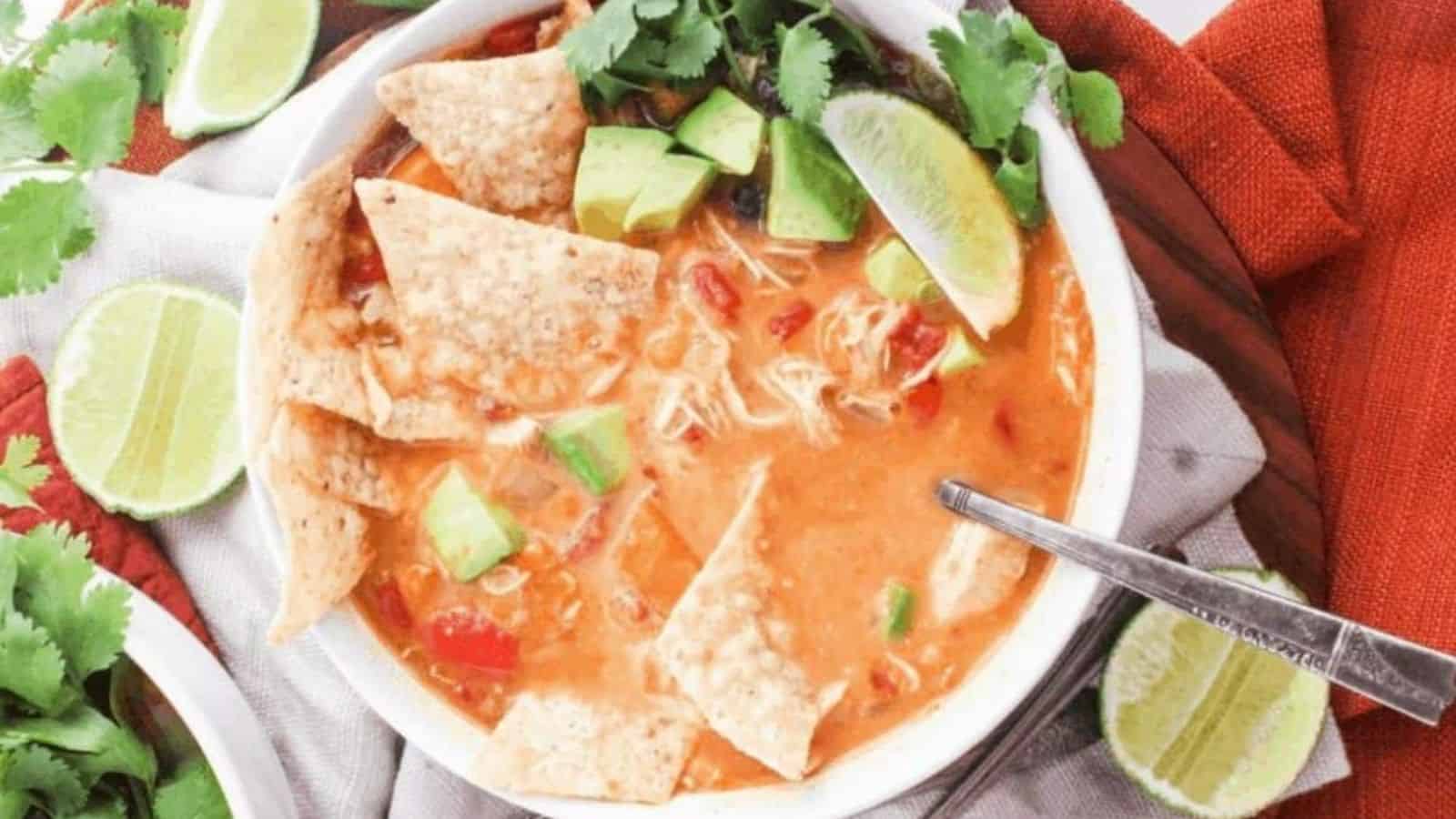 A bowl of chicken tortilla soup with tortilla chips, diced avocado, and sliced lime on top.