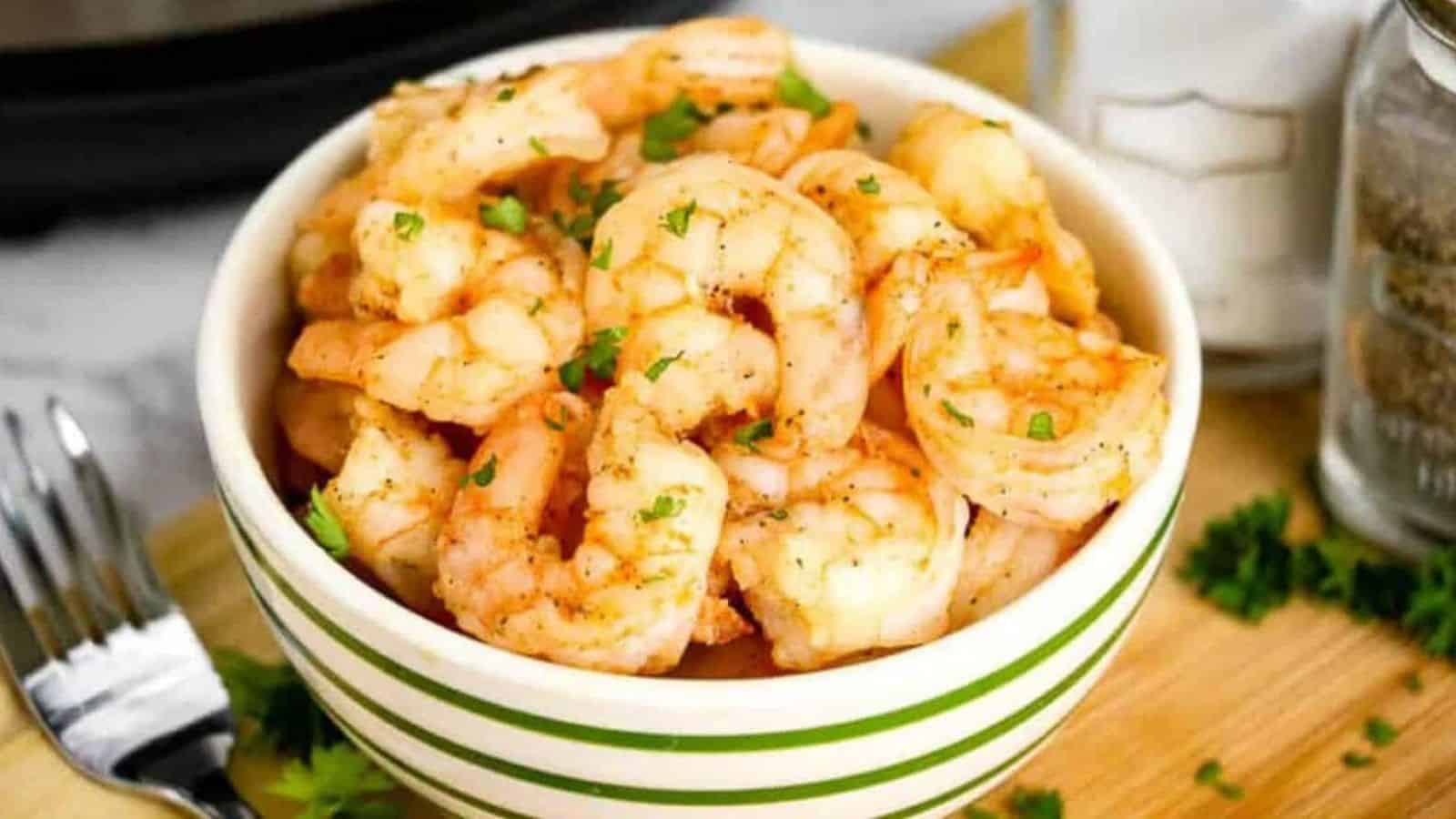 Cooked shrimp in a green and white striped bowl, garnished with parsley.