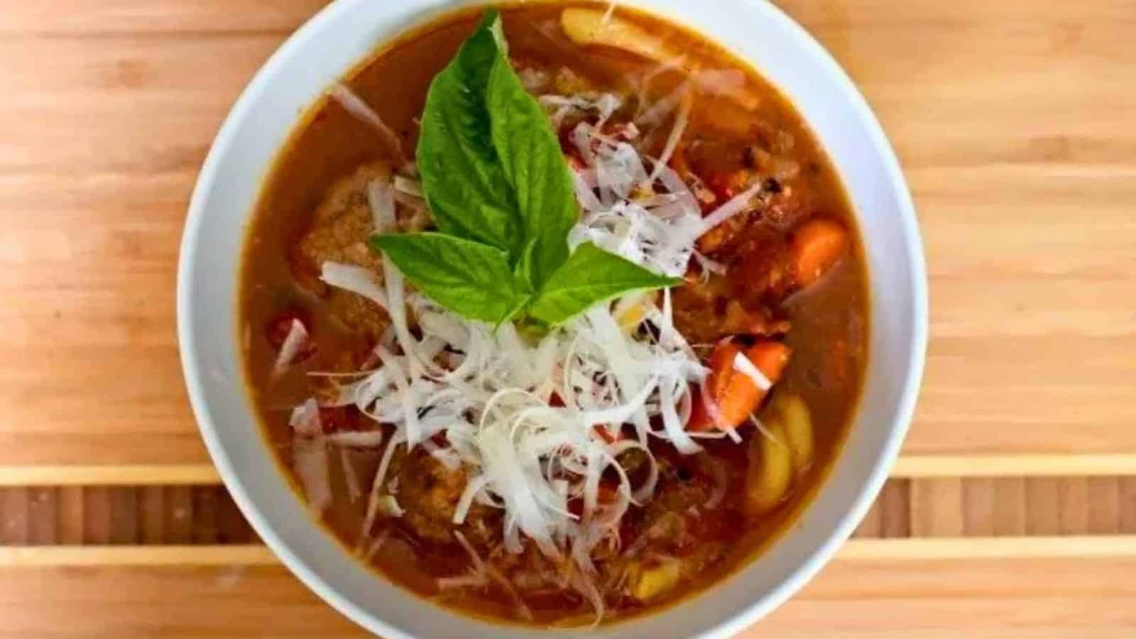 Image shows A bowl of italian meatball soup with a basil leaf on top.